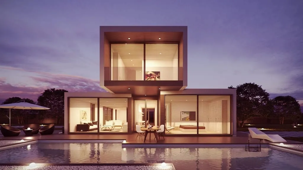 A modern Texas custom home glowing at dusk, glass upper volume above a lit lower level beside a still pool.