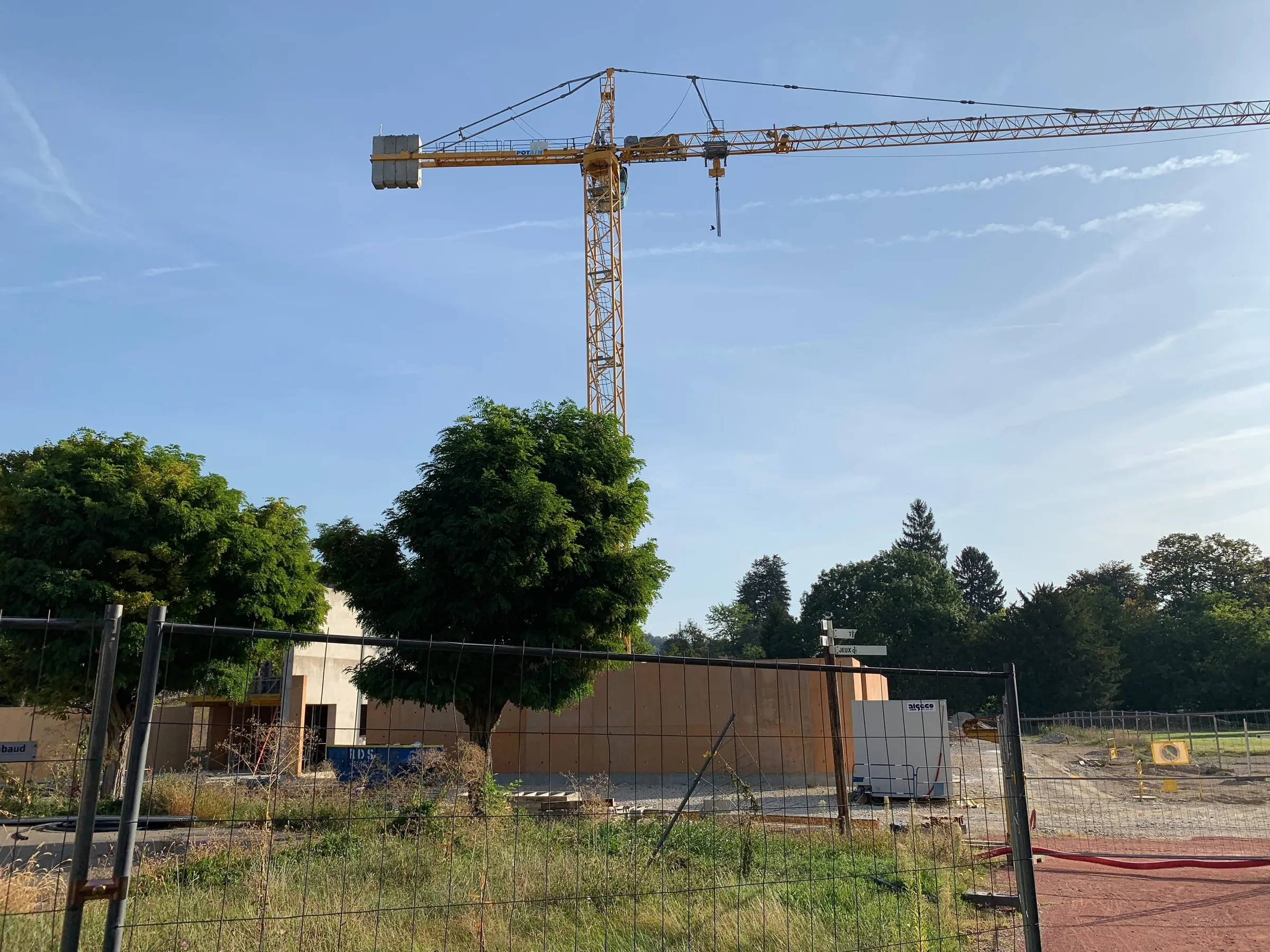 A tower crane rising over an active construction site under a clear sky.