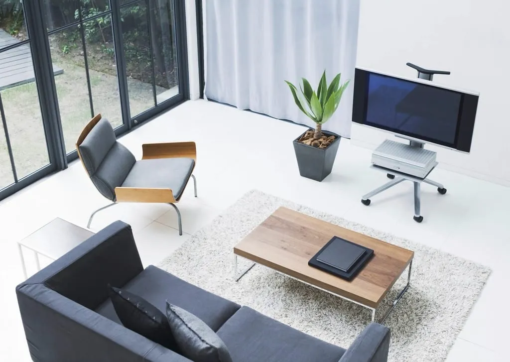 Bright modern office interior with lounge seating, a monitor on a stand, and full-height windows.