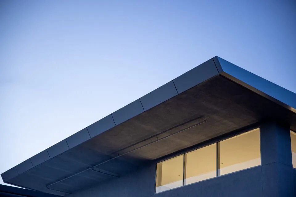 Underside of a modern home’s dark folded roofline against a clear blue Texas sky.