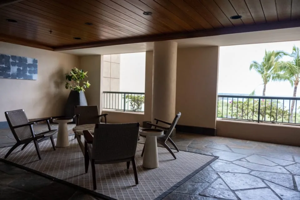Covered outdoor terrace with warm cedar ceiling, stone floor, and modern lounge chairs overlooking palms.